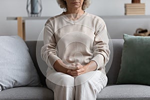 Worried concerned senior 60s lady keeping clasped hands on lap