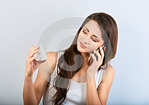 Worried confused young woman holding tablet bottle in the hand and calling on mobile phone to ask the doctor. She is looking on