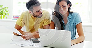 Worried couple calculating their bills with laptop in the kitchen