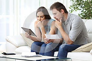 Worried couple comparing receipt on tablet at home photo