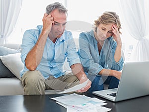 Worried couple paying their bills online with laptop