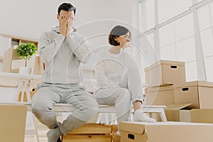 Worried couple pose near stack of cardboard boxes, have to move in other flat, have no money for rent, have dejected sad