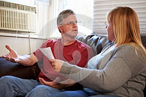 Worried Couple Sitting On Sofa Arguing About Bills