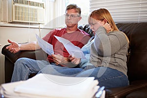 Worried Couple Sitting On Sofa Looking At Bills