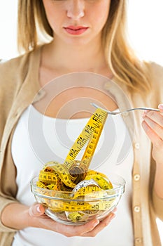 Worried cute woman holding bowl with measuring tapes at home