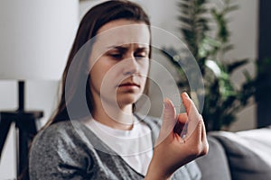 Worried depressed young woman holding wedding ring sitting alone on couch, breaking off engagement, ending relationship, abandoned