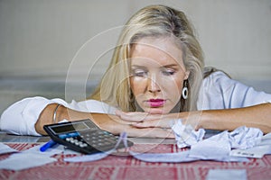 Worried and desperate blond woman calculating domestic money expenses doing paperwork and bank bills accounting with calculator su