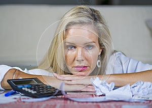 Worried and desperate blond woman calculating domestic money expenses doing paperwork and bank bills accounting with calculator su