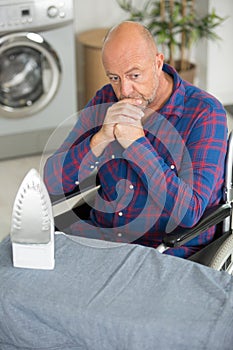 Worried disabled man sitting on wheelchair during ironing