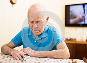 Worried elderly man measuring himself oxygen saturation at home