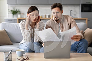 Worried european couple with documents and laptop at home