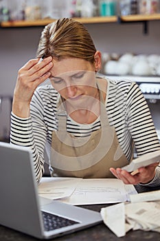 Worried Female Owner Of Coffee Shop In Financial Difficulty Looking Through Bills Using Laptop And Calculator