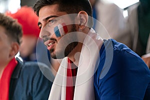 Worried football fans supporting French national team in live soccer match at stadium.