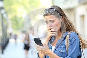 Worried girl checking smart phone in the street