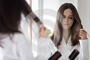 Worried girl concerned about hair loss, combing at mirror