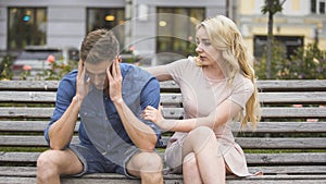 Worried guy sitting on bench, girlfriend calming him down, problems and support