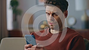 Worried guy texting message on smartphone at sofa close up. Tensed man messaging