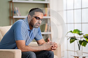Worried indian man in deep thinking while sitting on sofa at home - concept of financial problem, love breakup and
