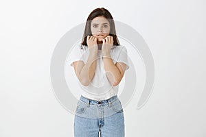 Worried intense cute caucasian woman in trendy jeans and t-shirt, clenching fists near face and biting lip, gazing