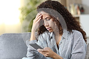 Worried latin woman reading on phone bad news