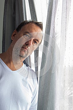 Worried looking adult man looking at camera next to a window