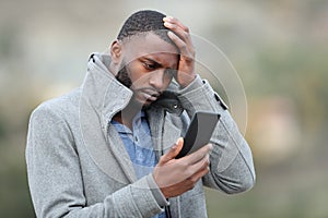 Worried man with black skin checking phone in winter