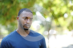 Worried man with black skin distracted looking away in a park
