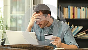 Worried man buying online with credit card and laptop