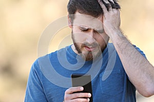 Worried man checking smartphone outdoors