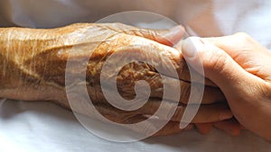 Worried man holding and gently stroking hand of his sick grandmother showing care or love. Son comforting wrinkled arm