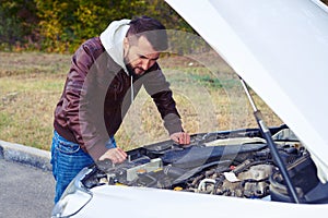 Worried man looking under the hood of car