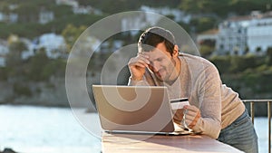 Worried man paying online with laptop and credit card