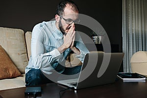 Worried man reading bad news on the laptop computer while working remotely at home.