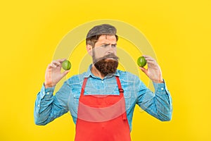 Worried man in red apron looking at fresh limes citrus fruits yellow background, fruiterer photo