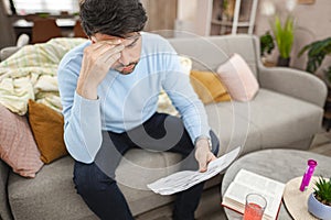 worried man sitting on couch looking at bills