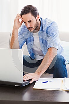 Worried man sitting at table using laptop to pay his bills