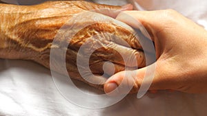 Worried man taking and gently stroking hand of his sick mother showing care or love. Son comforting wrinkled arm of