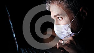 Worried man wearing face mask looks through a news site on his laptop. Latest coronavirus outbreak information related