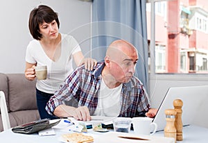 Worried man working at laptop and financial documents, woman helping