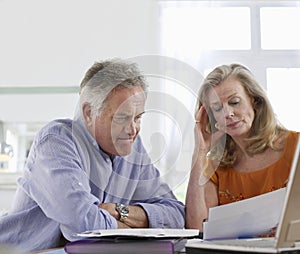Worried Mature Couple With Bills At Dining Table