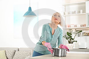 Worried mature woman collecting water leakage from ceiling at home