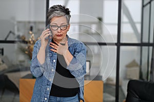 Worried mature woman talking on the phone in home interior