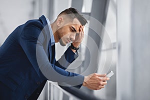 Worried middle-eastern businessman looking at smartphone screen while waiting at airport terminal