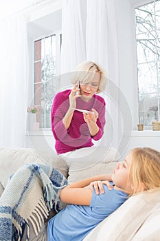 Worried mom calling doctor holding thermometer in hand.