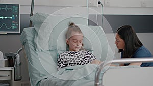 Worried mother sitting beside little daughter praying while sleeping after illness surgery