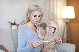 Worried mother takes temperature to sick crying baby at home