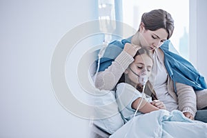 Worried mother taking care of her daughter wearing an oxygen mas