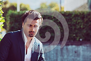 Worried and pensive man outdoors in a park. Fixed gaze downward. Intense daylight