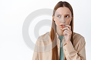 Worried pensive teen student look aside, touching lip nervously and thinking, standing anxious or hesitant against white