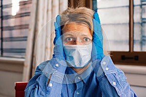 Worried person with virus protection surgical face mask and gloves holding her hea